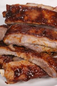 A close-up of several pieces of glazed Instant Pot barbecue ribs stacked on a plate, showcasing tender baby back ribs ready to savor.