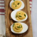 A platter of spicy deviled eggs garnished with paprika and chives.