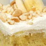 Close-up of a banana cream cake slice topped with whipped cream, banana slices, and crumbled cookies.