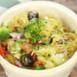 A bowl of California Spaghetti Salad with spaghetti squash, chopped vegetables including broccoli, black olives, red bell peppers, and herbs.