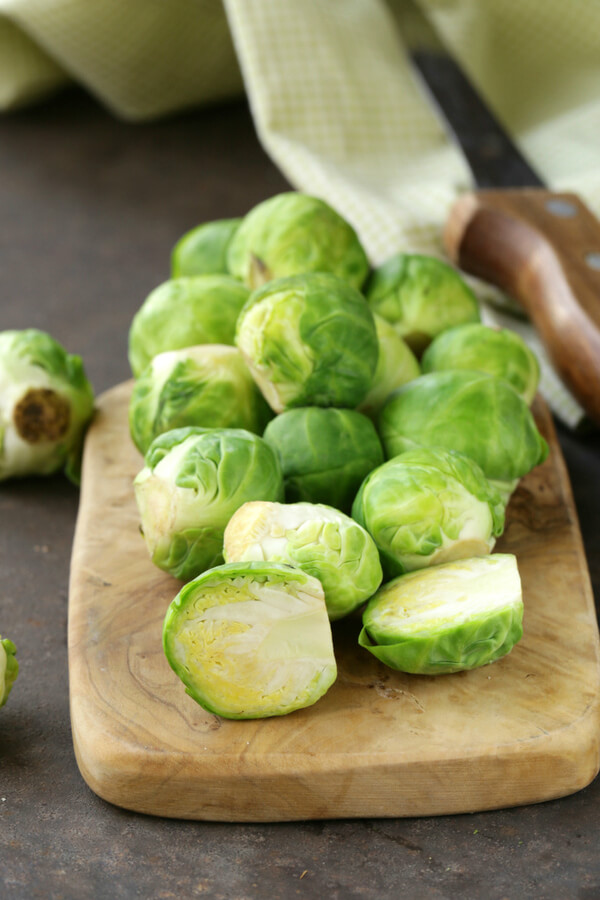 Brussel sprouts on a wooden cutting board, with a metal and a yellow napkin.  