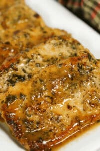 Close-up of seasoned and cooked salmon fillets with a herb glaze, artfully arranged beside pan-seared pork chops, served on a pristine white plate.