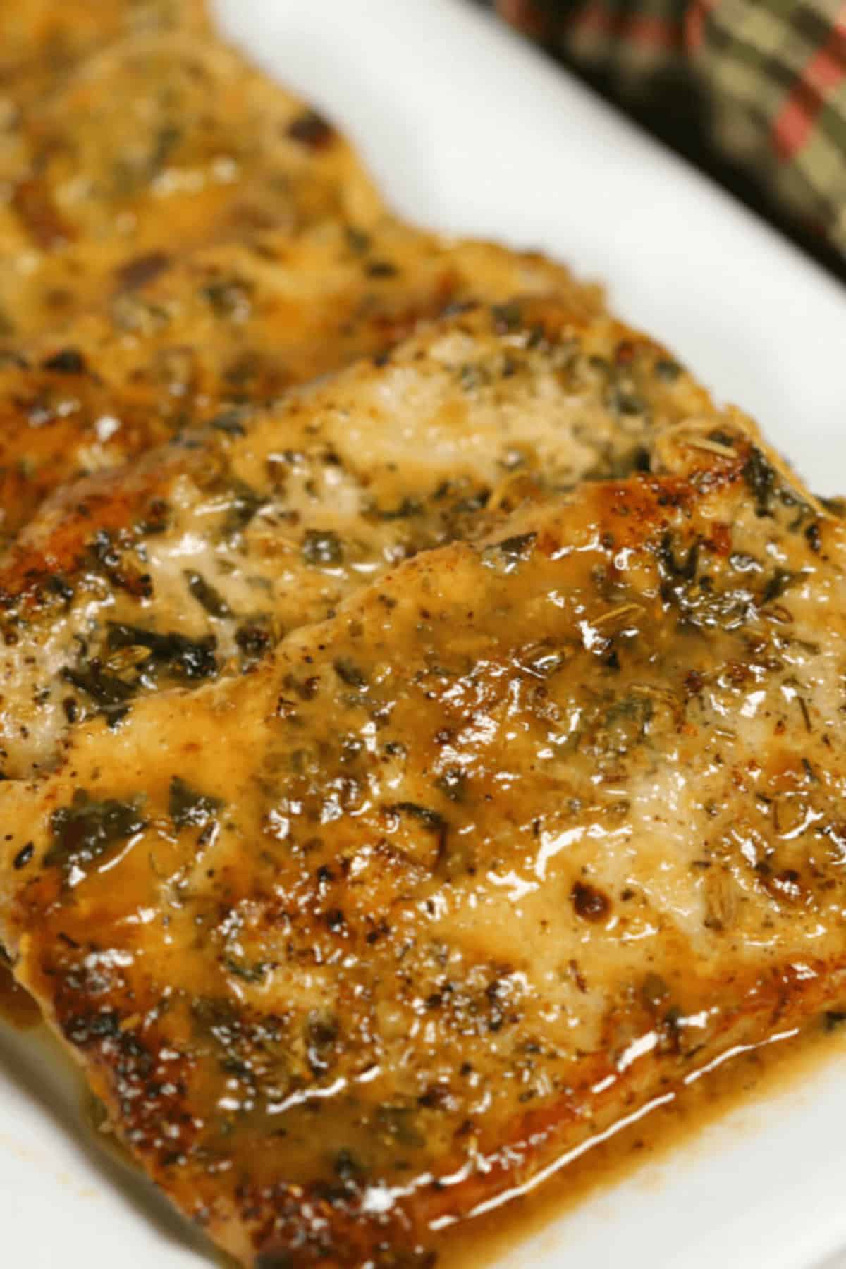 Close-up of seasoned and cooked  fillets with a herb glaze, artfully arranged beside pan-seared pork chops, served on a pristine white plate.