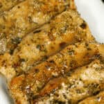 Slices of seasoned, cooked meat arranged in a row on a white plate, reminiscent of the savory elegance.