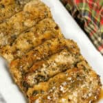 Pan seared pork chops, glazed to perfection, are artfully arranged on a white rectangular plate with a plaid cloth in the background.