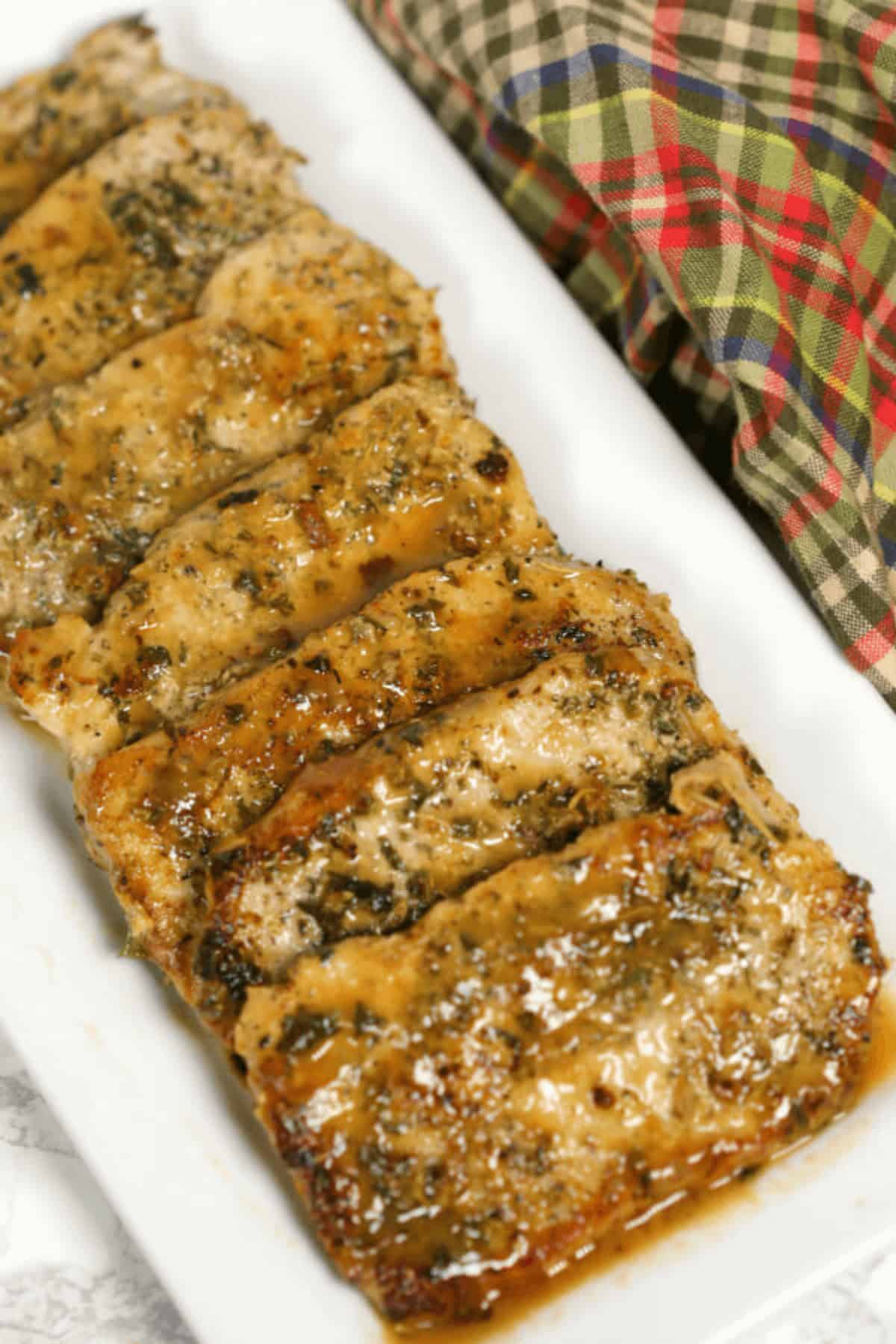 Pan seared pork chops, glazed to perfection, are artfully arranged on a white rectangular plate with a plaid cloth in the background.