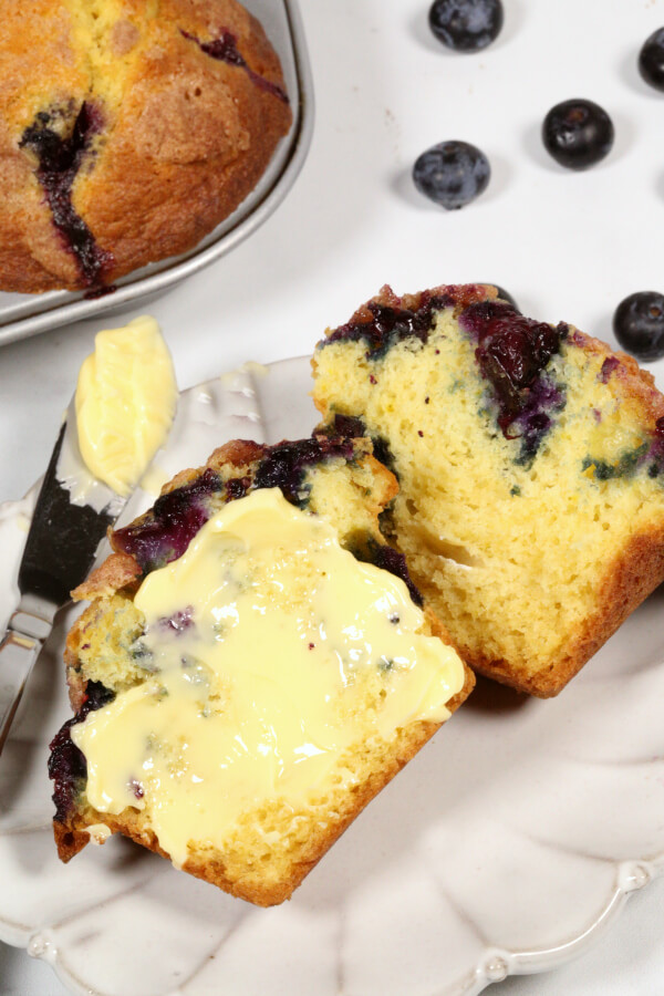 blueberry streusel muffins with honey butter on a white plate with a silver knife.