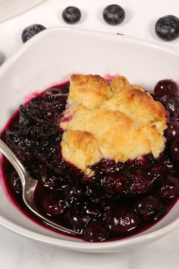 Blueberry Cobbler in a white bowl with a silver spoon.