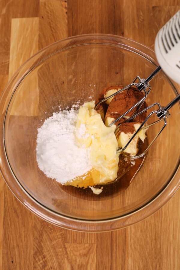 Powdered sugar, honey, salt, cinnamon and butter being hand mixed in a large clear bowl 