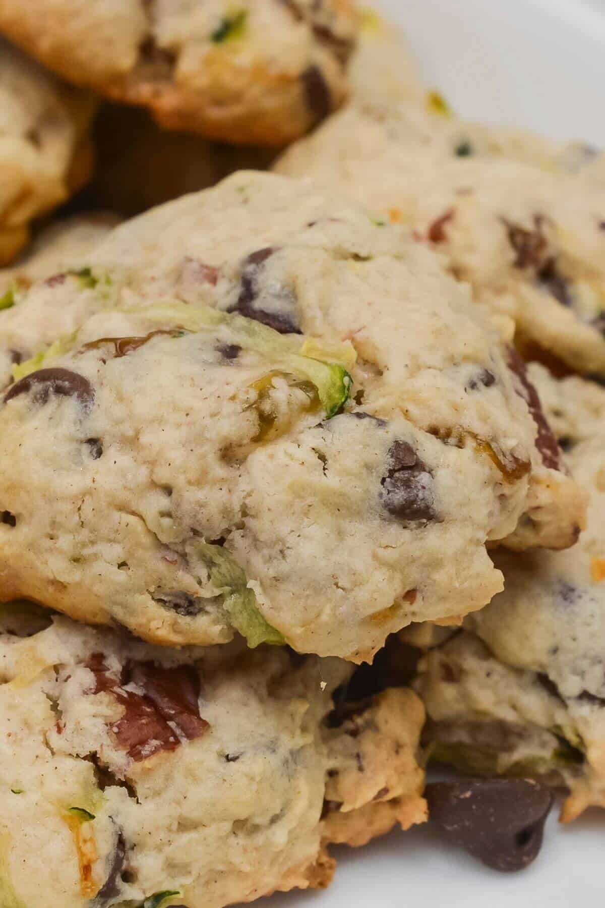 A close-up of chunky zucchini cookies with visible chocolate chips and green pieces, stacked on a white plate.