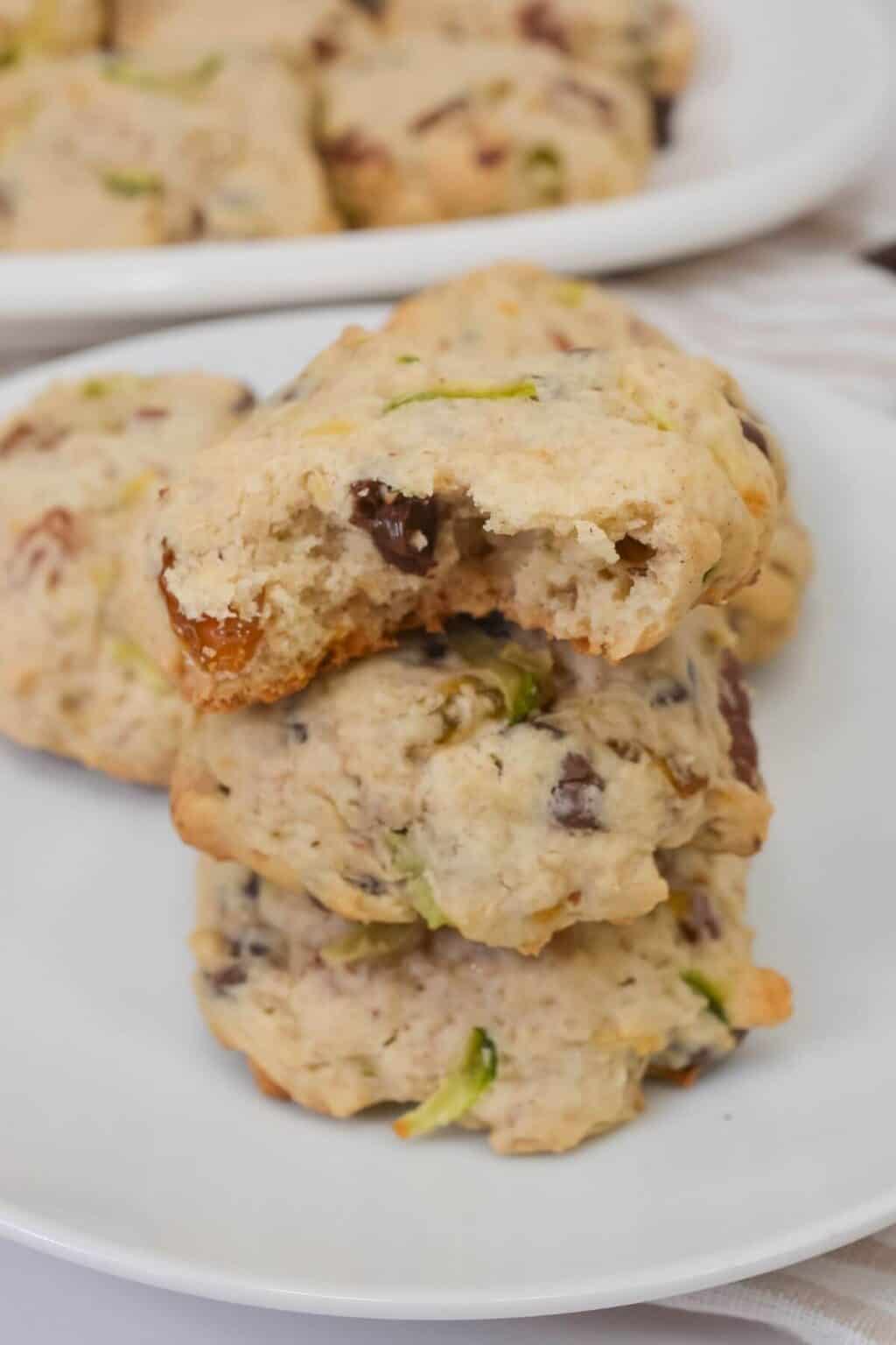 A stack of three with visible chocolate chips and green pieces, one with a bite taken out, sits on a white plate with more in the background.