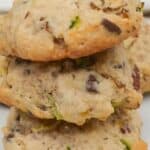 Three homemade Zucchini Cookies with visible chunks of chocolate and green zucchini are stacked on a white surface, with more cookies blurred in the background.