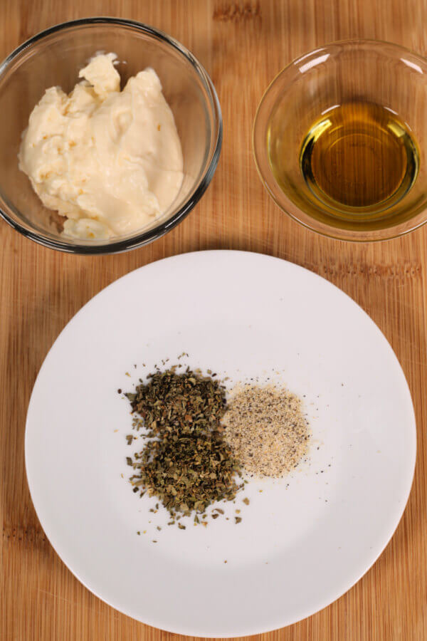 mayo in a clear bowl, clear bowl of olive oil, and basil and oregano on a white plate.