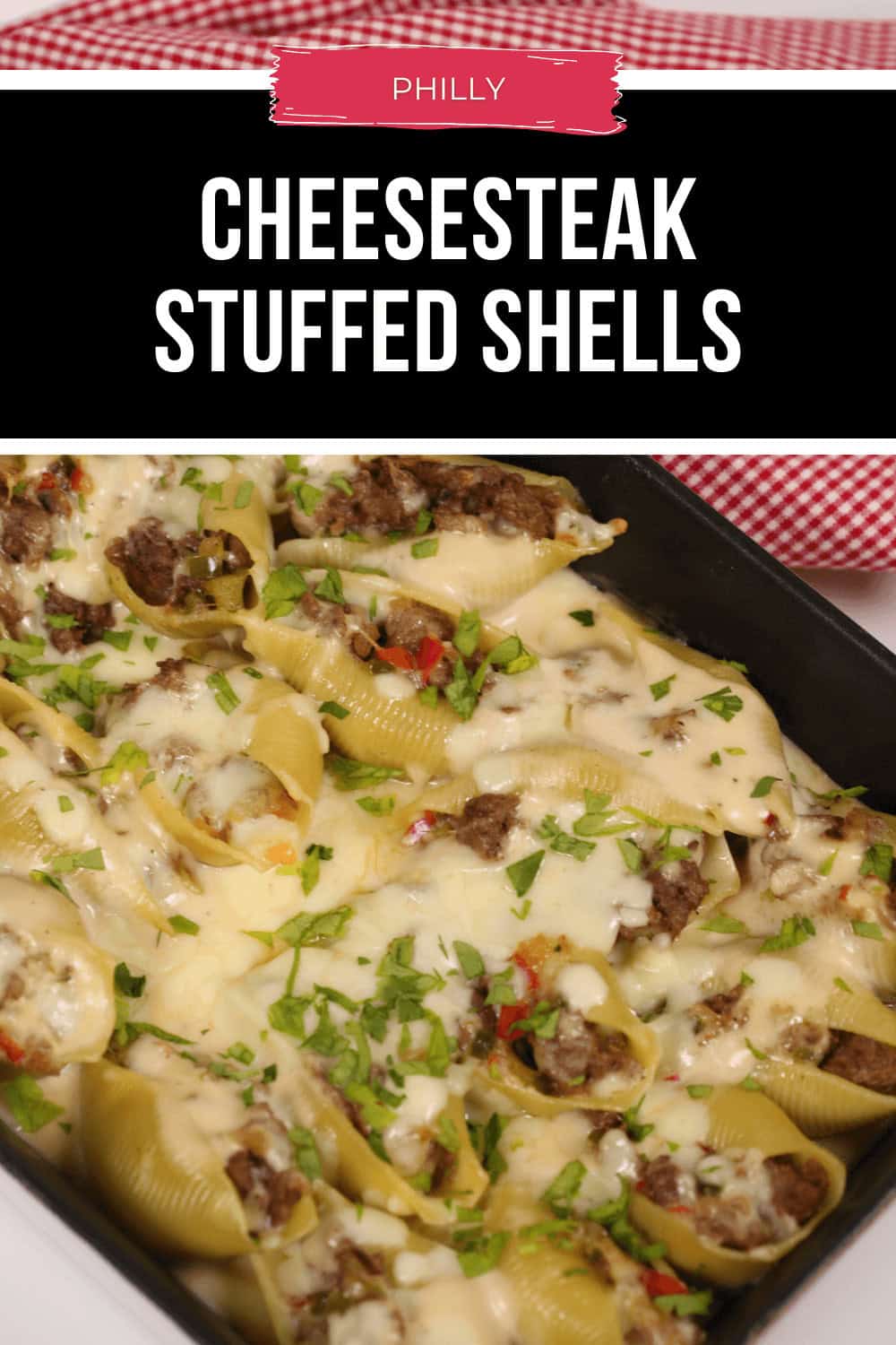 Baked Philly Cheesesteak Stuffed Shells topped with melted cheese and chopped herbs in a black baking dish.
