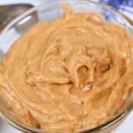 A close-up of a glass bowl filled with Texas Roadhouse Butter, with a spoon partially visible in the background.