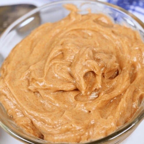 A close-up of a glass bowl filled with Texas Roadhouse Butter, with a spoon partially visible in the background.