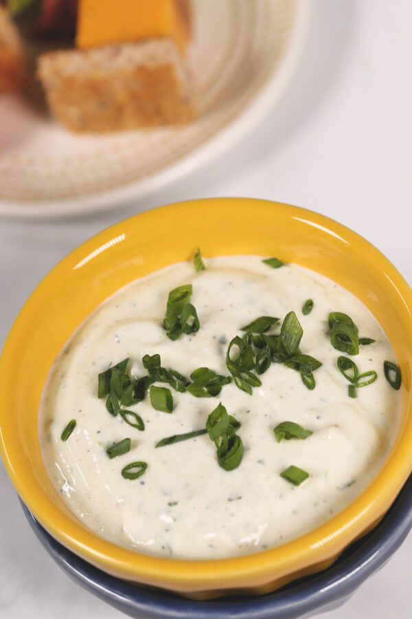 Yogurt ranch dressing topped with green onion in a yellow bowl 
