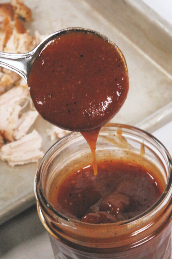 apple cider bbq sauce in mason jar with a scoop in a measuring cup.