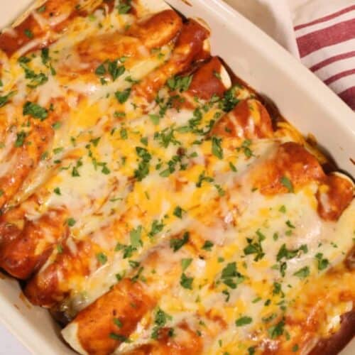A casserole dish filled with ground beef enchiladas topped with melted cheese and fresh herbs.