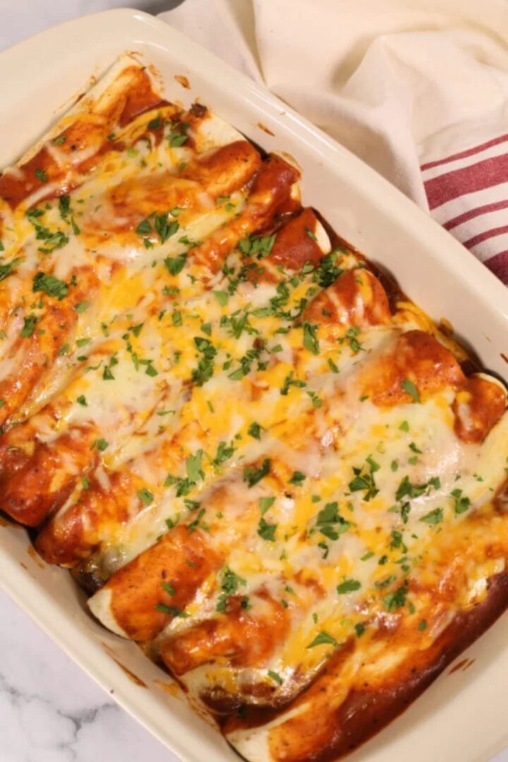 A casserole dish filled with ground beef enchiladas topped with melted cheese and fresh herbs.