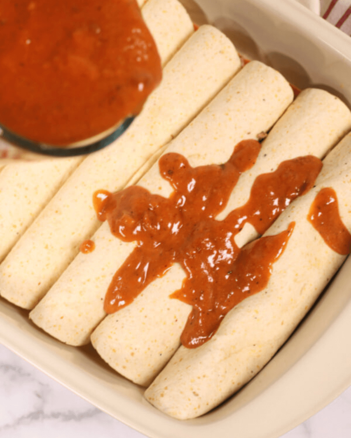 A dish of chicken enchiladas topped with red sauce, arranged neatly in a white rectangular baking dish.