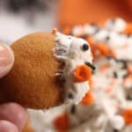 A hand holds a cookie, dipped in white frosting with orange and black sprinkles.