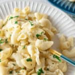 A plate of pasta with a creamy white sauce, reminiscent of homemade Instant Pot Mac n Cheese, is garnished with chopped parsley and sits invitingly on a white plate. A fork elegantly holds a tempting portion of the pasta.