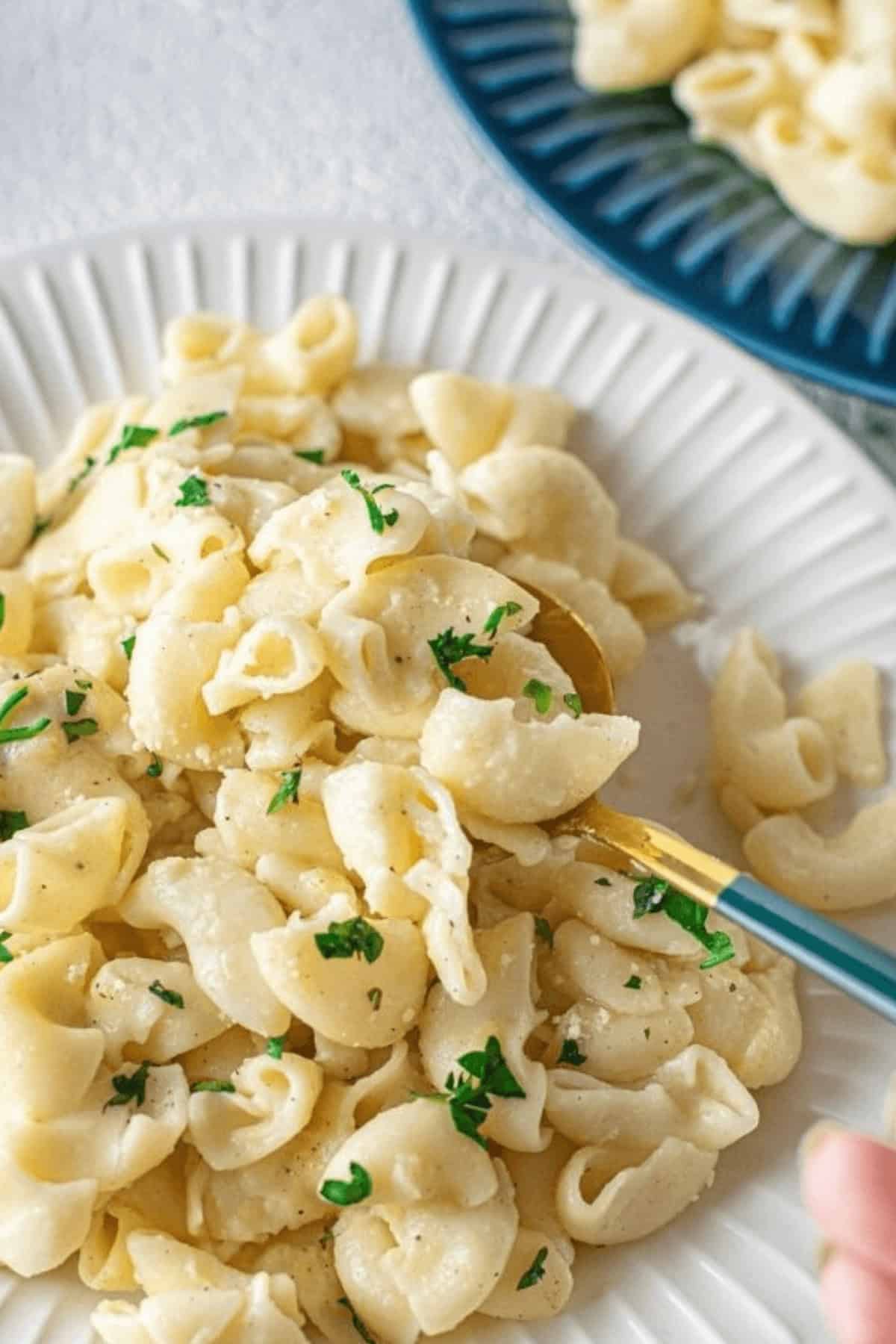 A plate of pasta with a creamy white sauce, reminiscent of homemade Instant Pot Mac n Cheese, is garnished with chopped parsley and sits invitingly on a white plate. A fork elegantly holds a tempting portion of the pasta.