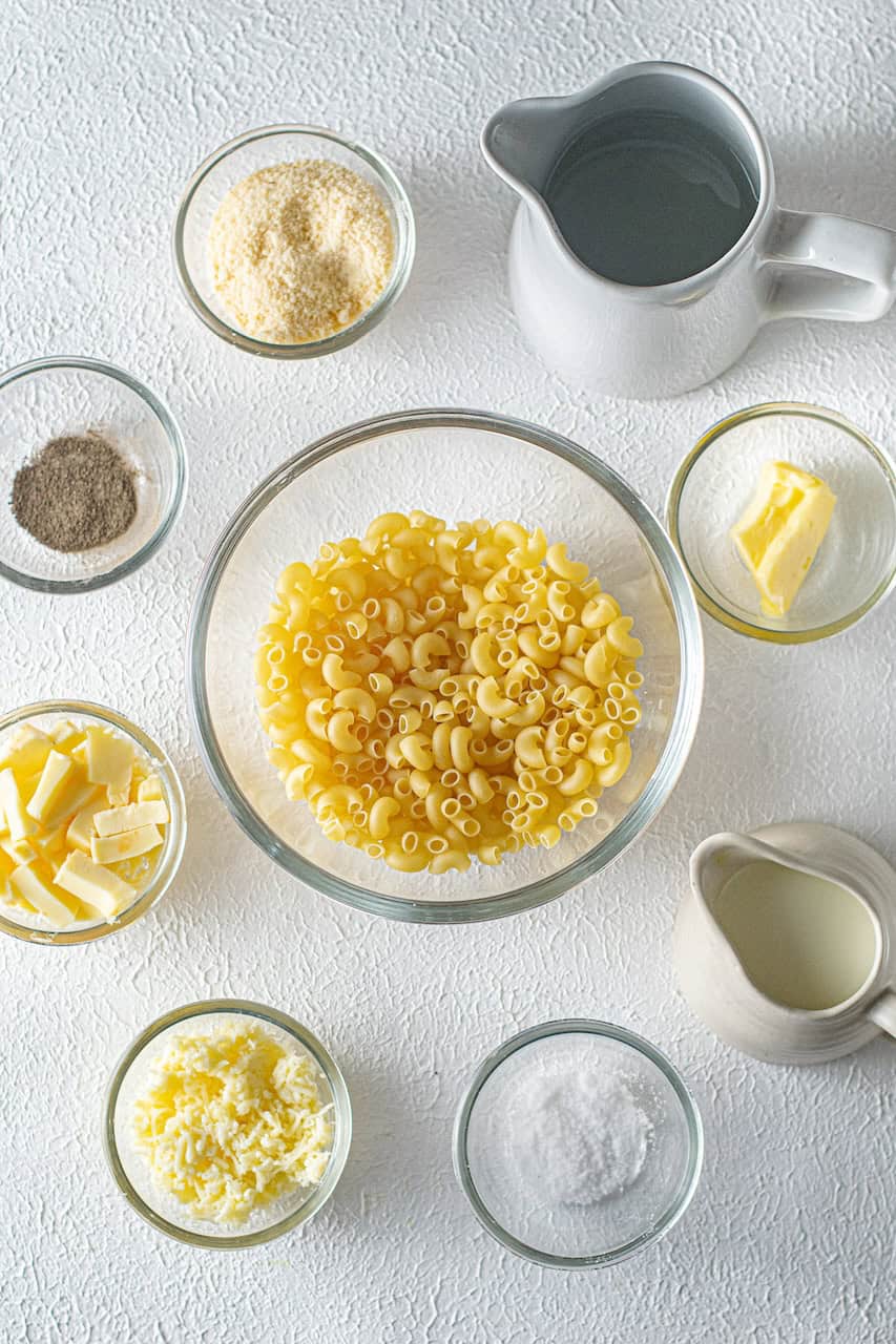 Ingredients for Instant Pot Mac n Cheese arranged on a white surface include macaroni, cheese, butter, milk, water, salt, and pepper.