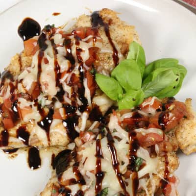 Bruschetta chicken on a white plate with a red napkin and silverware