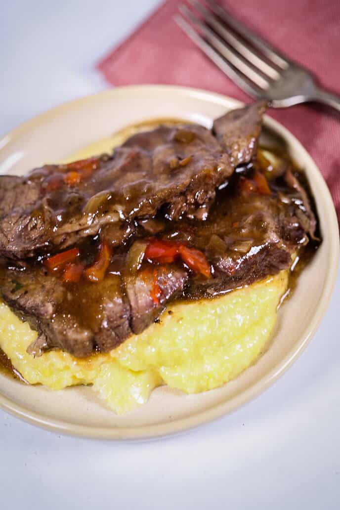 Creamy polenta on a plate with Italian beef on top of it