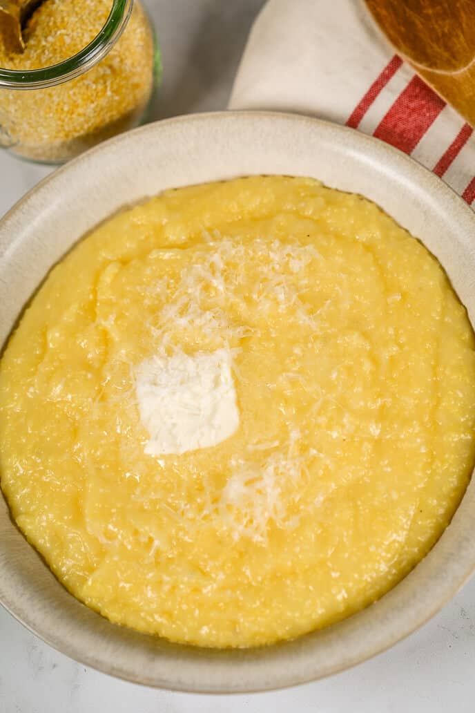 Creamy polenta in a bowl with a striped napkin and wooden spoon