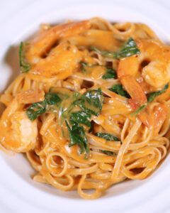 A plate of Tuscan shrimp pasta with spinach in a creamy sauce.
