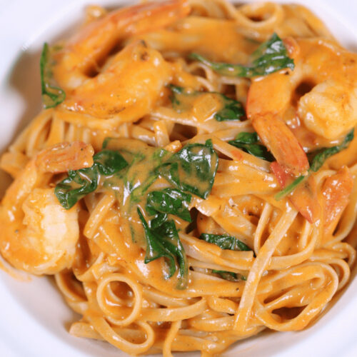 A plate of Tuscan shrimp pasta with spinach in a creamy sauce.
