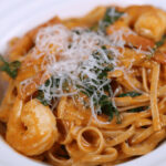 A bowl of Tuscan shrimp pasta, garnished with grated cheese and herbs.