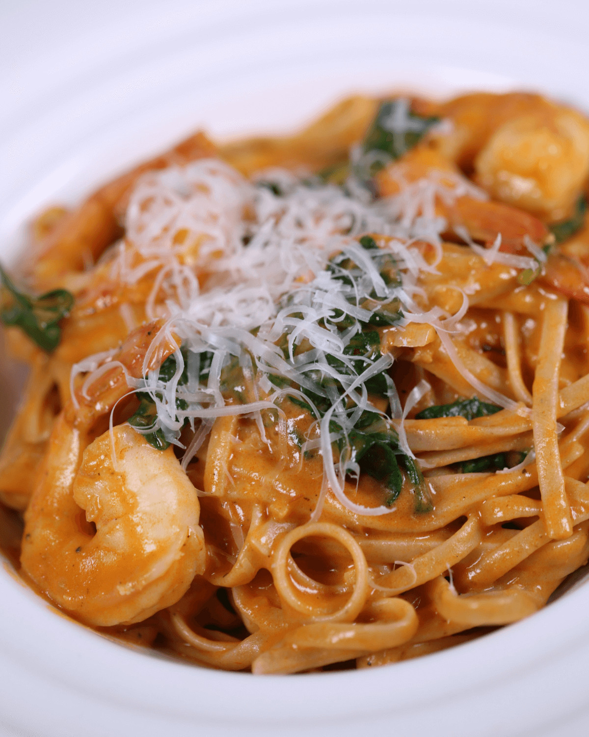 A bowl of Tuscan shrimp pasta, garnished with grated cheese and herbs.