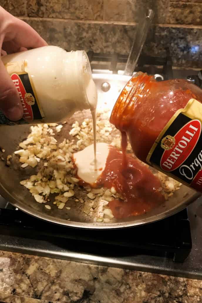 Bertolli alfredo sauce mixing with Bertolli Tomato and Basil Sauce in a skillet with onions