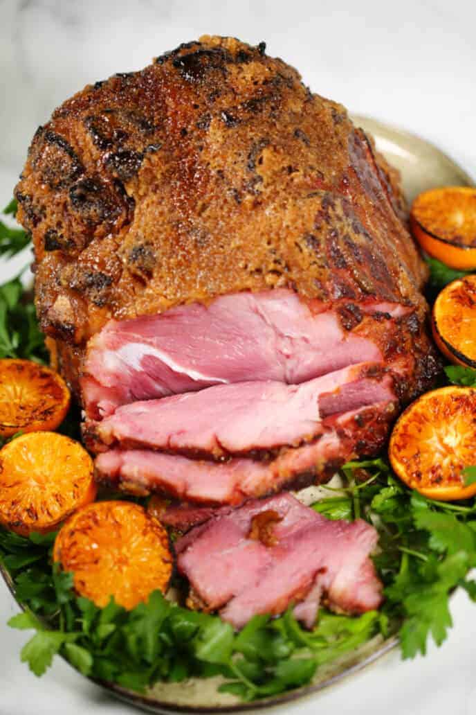 Honey baked ham recipe on a platter with greens and oranges