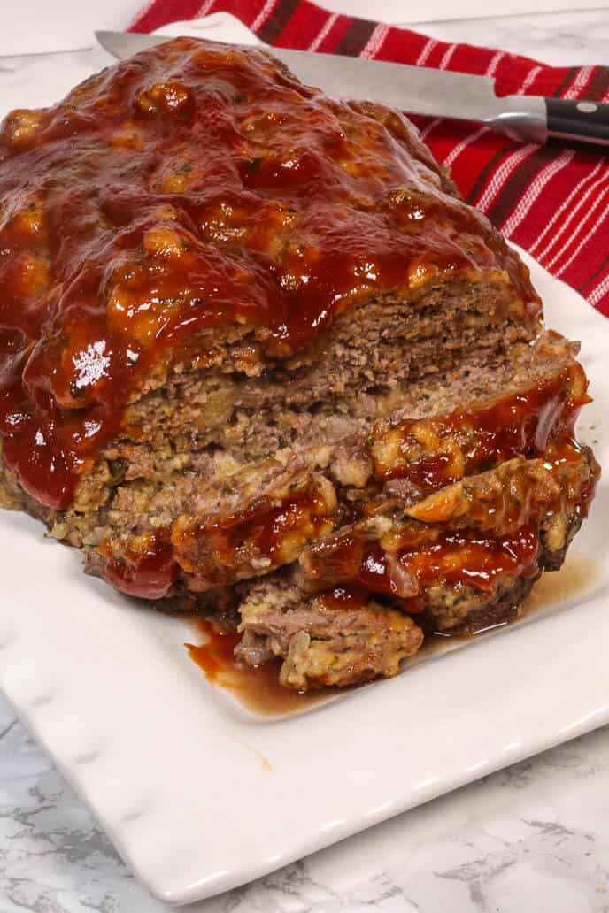 Instant Pot Meatloaf on a white platter with a red striped napkin and a steak kneef