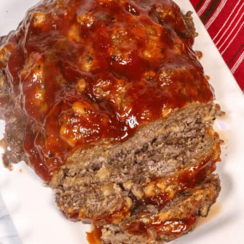 The dinner served on a white rectangular plate. A knife and a red-striped cloth are in the background.