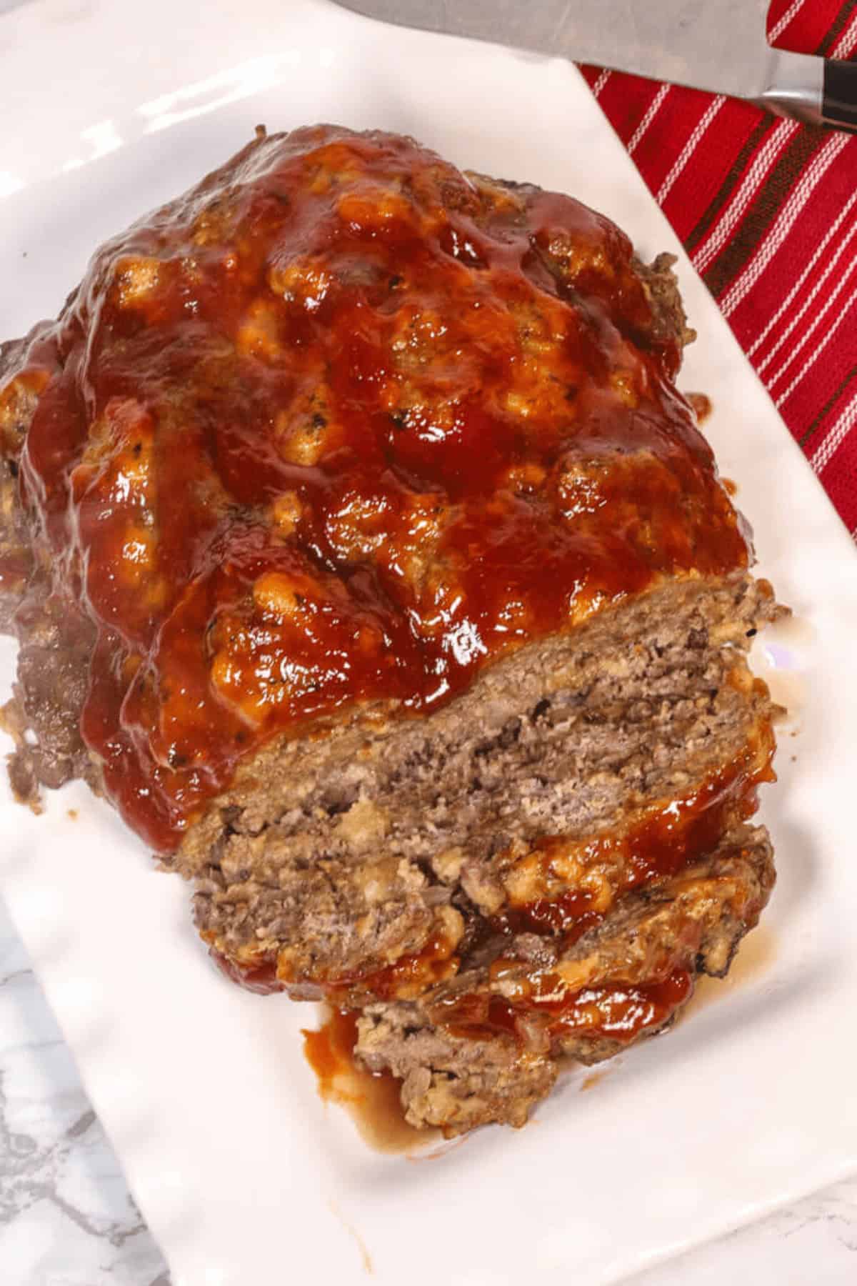 The dinner served on a white rectangular plate. A knife and a red-striped cloth are in the background.