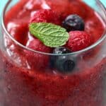 A glass filled with a blended Mixed Berry Smoothie, topped with whole raspberries, blueberries, and a fresh mint leaf.