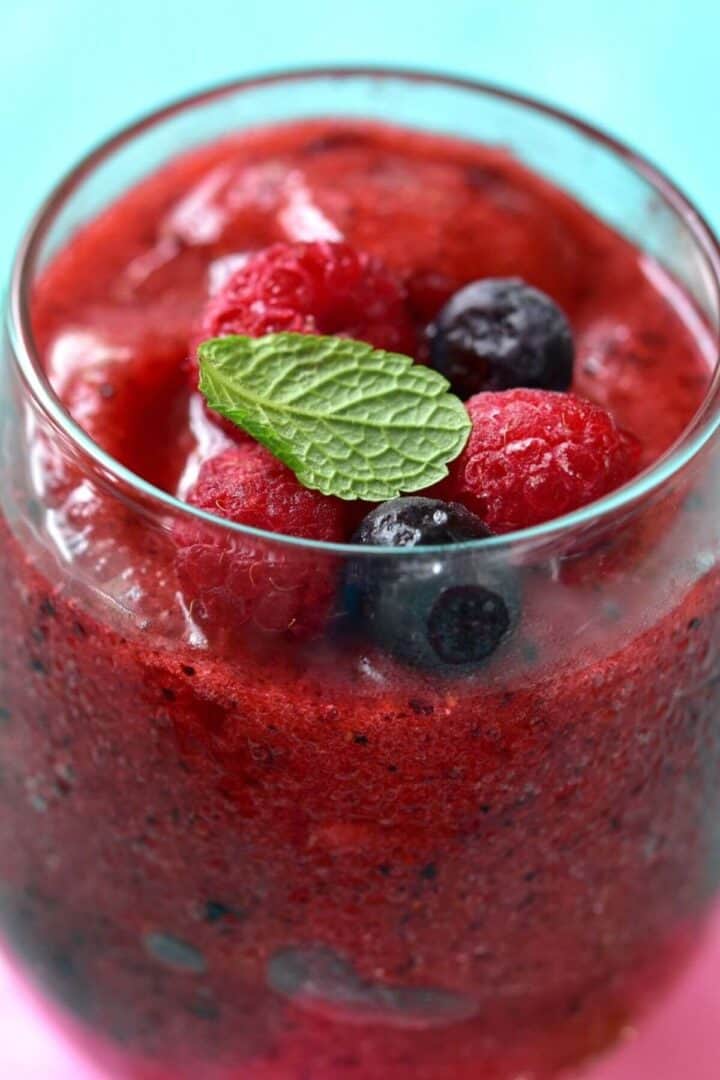 A glass filled with a blended Mixed Berry Smoothie, topped with whole raspberries, blueberries, and a fresh mint leaf.