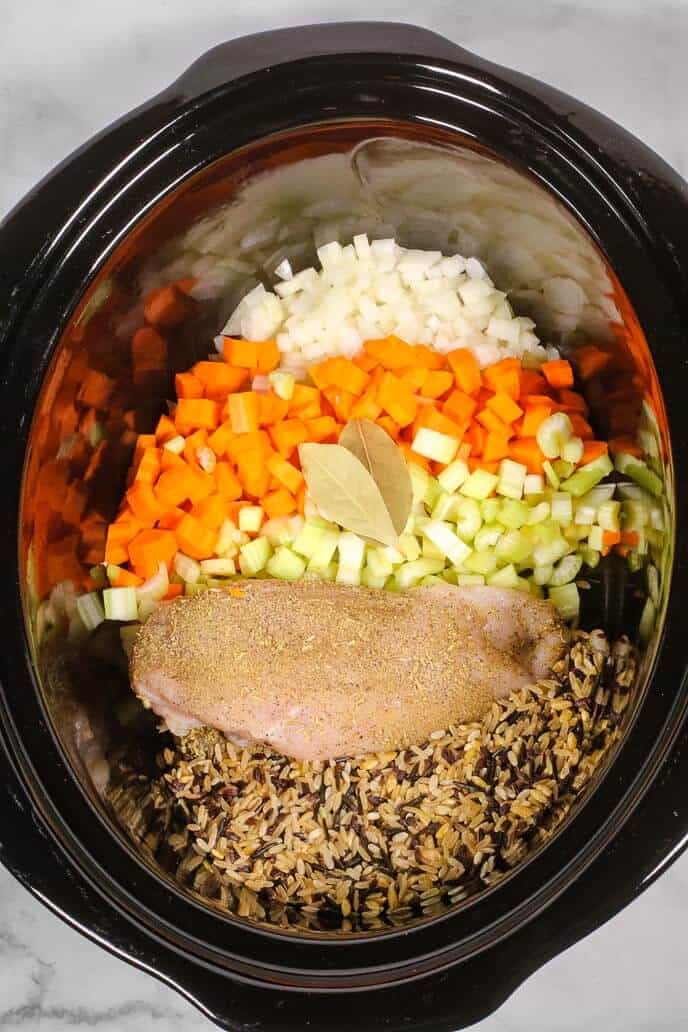 Crock pot with the ingredients for chicken and wild rice soup