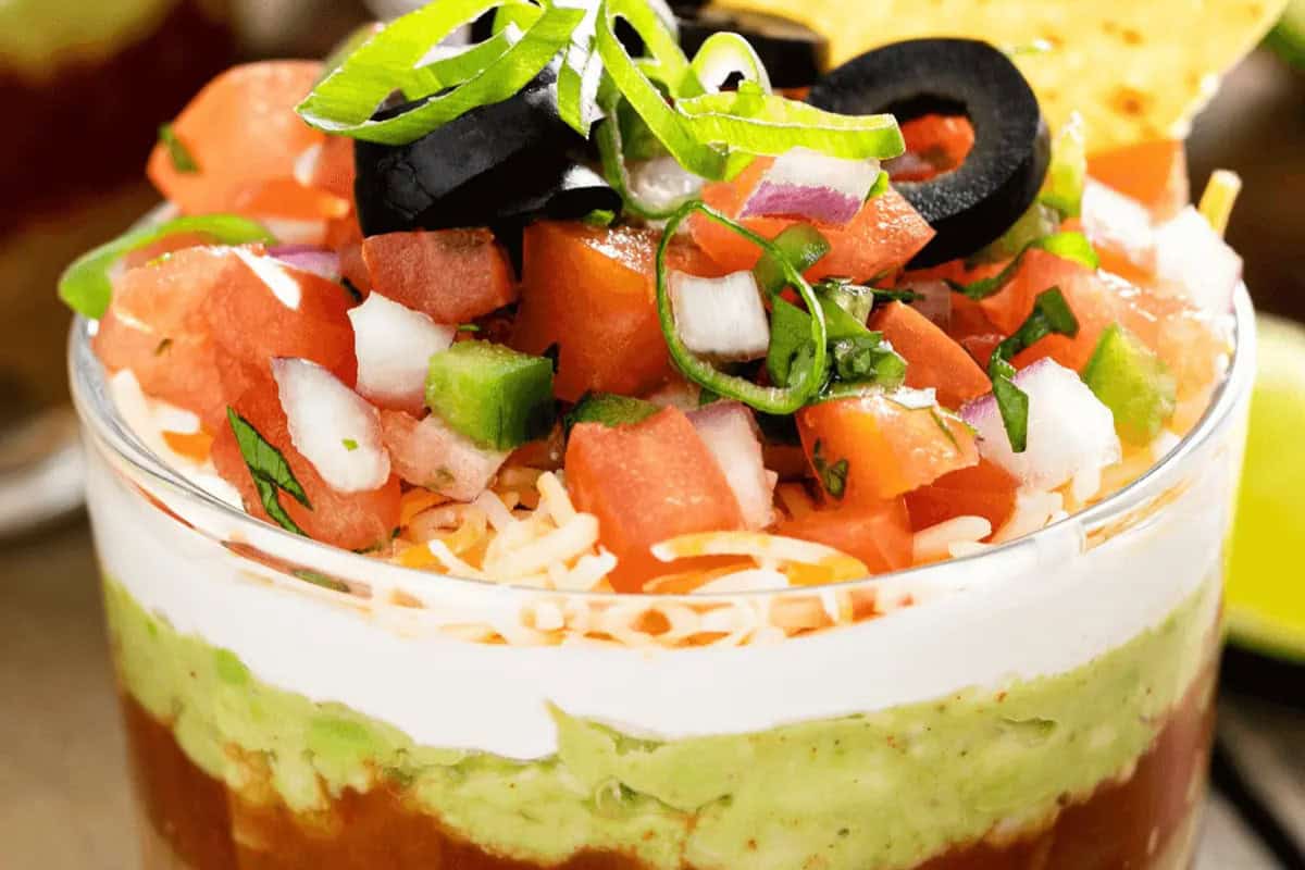 Celebrate with a festive layered dip, perfect for Cinco de Mayo food gatherings. Featuring beans, guacamole, sour cream, shredded cheese, diced tomatoes, onions, bell peppers, sliced black olives and green onions—all crowned with a crisp tortilla chip.