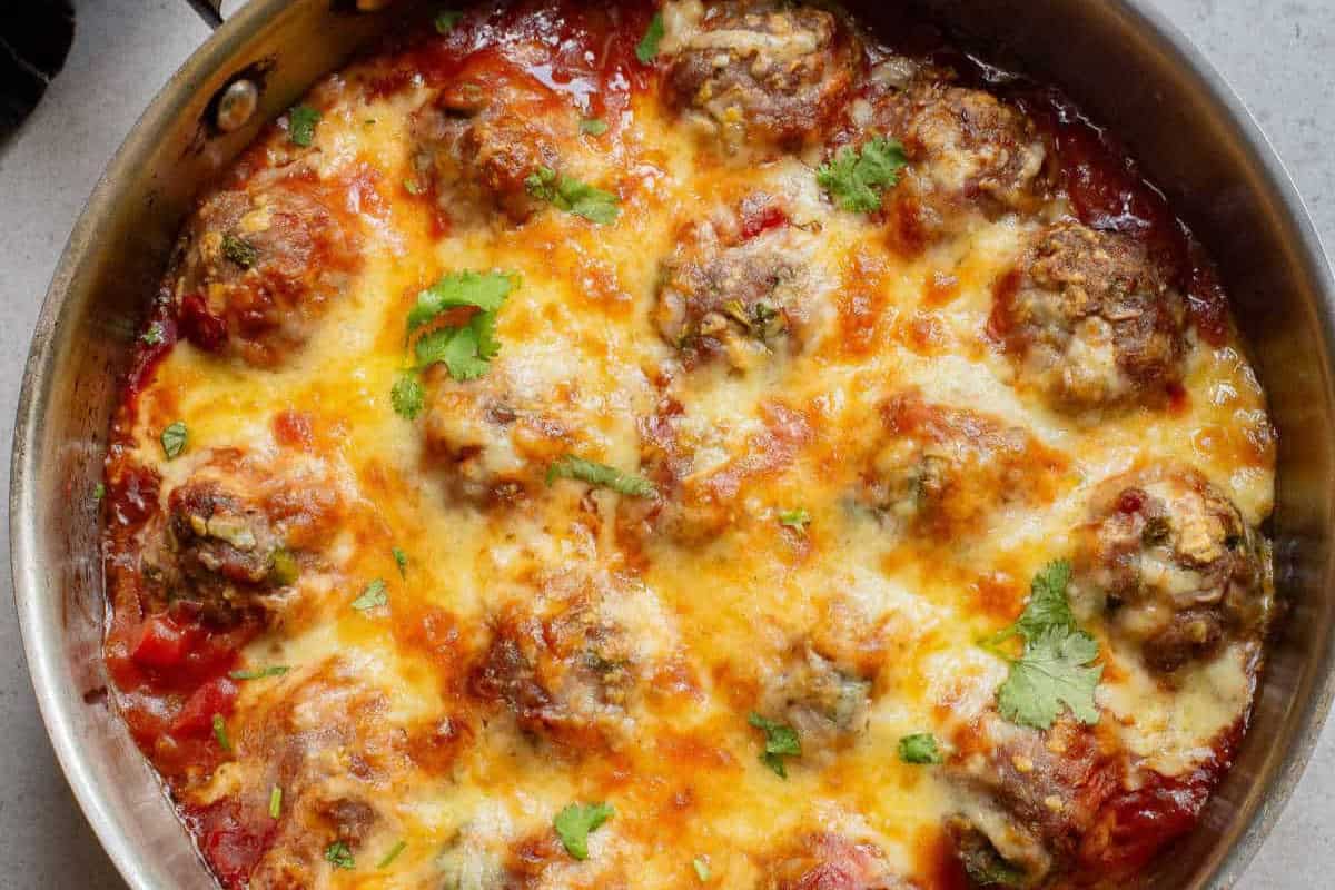 A pan of meatballs covered in melted cheese, garnished with cilantro in a tomato-based sauce, perfect for Cinco de Mayo celebrations.