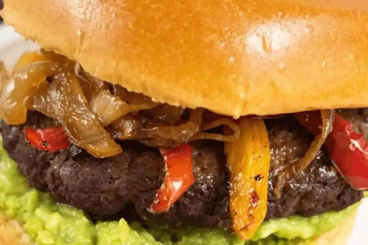 Close-up of a burger with caramelized onions, red peppers, and avocado on a bun, perfectly capturing the vibrant flavors of Cinco de Mayo food.