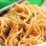 A bowl of cold sesame noodles garnished with chopped green onions.