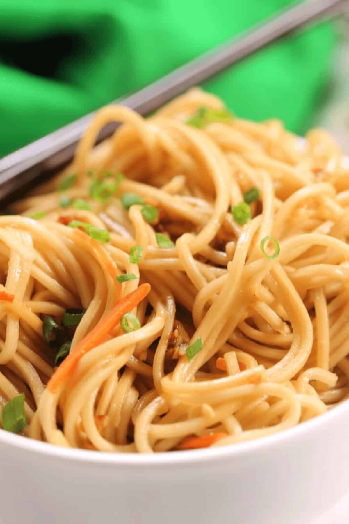 A bowl of cold sesame noodles garnished with chopped green onions.