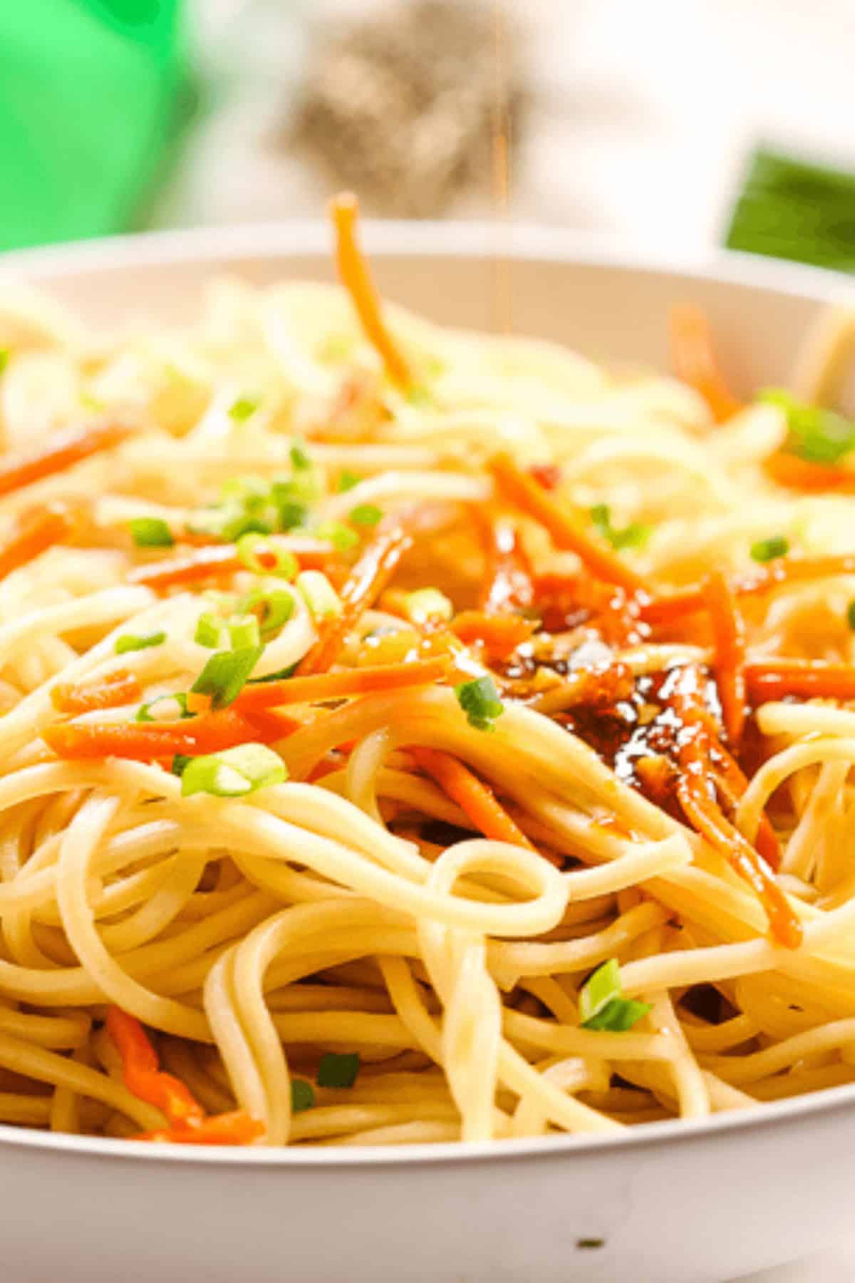 Close-up of a bowl of cold sesame noodles garnished with chopped green onions and vibrant orange strips on top.